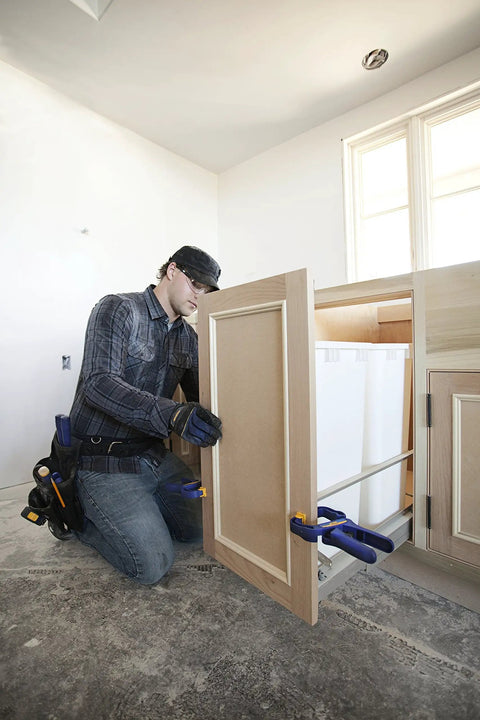 Carpenter using Heavy Duty Four Piece Clamp Set With Two Four And A Half Inch Bar Clamps And Two Two Inch Handi Clamps for cabinet installation.