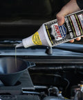 Pouring Pure Synthetic Motor Oil Stabilizer Formula into a funnel over an engine for smooth operation and pressure maintenance.