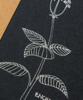 Cardstock with white debossed plant illustration on black surface; kraft backing visible