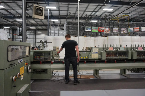 Factory worker operating machinery in production line under industrial lighting, managing controls for manufacturing process.