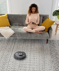 Robot Vacuum With Matrix Clean And Precision Mapping Self Empty Base With 30 Day Capacity Bagless Powerful Pet Hair Cleaning WiFi Enabled Black Renewed vacuuming a carpeted room with a woman sitting on a couch.