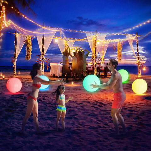 Family playing with 16 Inch Light Up Glow Beach Ball With 8 LED Modes For Night Pool Fun on a beach at sunset, colorful balls lit.