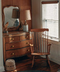 Vintage wooden dresser with antique brass knobs next to a wooden chair, enhancing retro charm in a cozy interior setting.