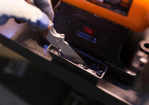 Eight Inch Bench Grinder Powered By A Beefy Four Point Eight Amp Motor Hitting 3450 RPM, Features Adjustable Eye Guards With Bright LED Work Lights And Cooling Tray, Straight Up Shop Essential For Knife Sharpening And Metal Jobs, showing a person sharpening a knife over the cooling tray.