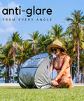 Woman using Outdoor Laptop Sun Shade For Working Anywhere Glare Blocker And Heat Reflective Hood on grass under palm trees