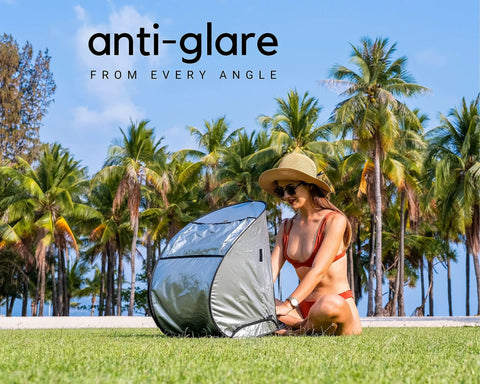 Woman using Outdoor Laptop Sun Shade For Working Anywhere Glare Blocker And Heat Reflective Hood on grass under palm trees