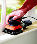 User operating Quarter Sheet Orbital Palm Sander Professional Grade 220 Watt Motor on wooden window sill.