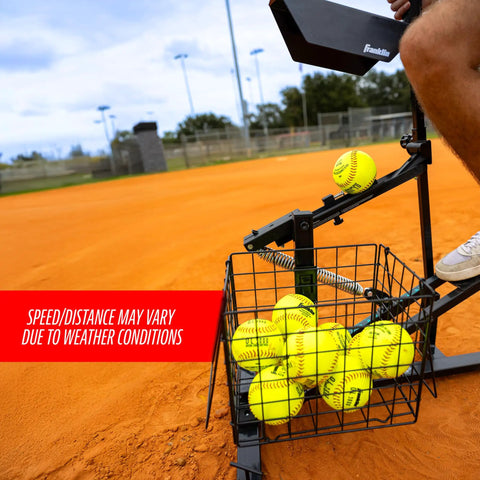 All In One Baseball And Softball Training Aid With Spring Loaded Ball Launcher For Batting And Grounders Battery Free Pitching Machine For Backyard Practice And Batting Cage Sessions showing yellow softballs in metal basket on field.
