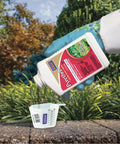 Gardener pouring Pyrethrin Garden Insect Spray Concentrate 8 Oz Ready To Mix Fast Acting Insecticide into measuring cup outdoors