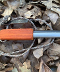 Compact European Fire Steel Ferro Rod with Magnesium on lanyard, resting on dry leaves, outdoor emergency fire starter setup.
