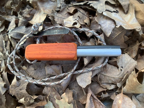 Compact European Fire Steel Ferro Rod with Magnesium on lanyard, resting on dry leaves, outdoor emergency fire starter setup.