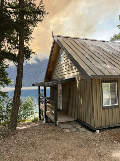 Wood cabin by lake with wildfire in background, demonstrating need for Wildfire Protection Sprinkler System with Bracket and Hardware.