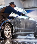 Person using 50 Ft High Pressure Washer Hose 3600 PSI Flexible And Kink Resistant Replacement With One Quarter Inch Quick Connect M22 Three Eighths Inch Adapters Heavy Duty Power Washer Extension Blue to clean a car in a garage setting.
