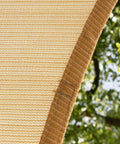Close-up of Beige Right Triangle Shade Sail Canopy 24x24x33.9 Ft, 200 GSM HDPE fabric edge with outdoor trees in background.