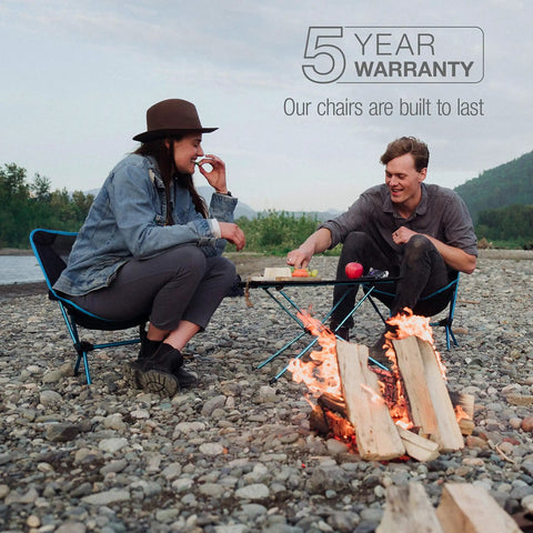 Lightweight Collapsible Camping Chair For Backpacking And Outdoors used by two people near campfire, 5-year warranty message visible
