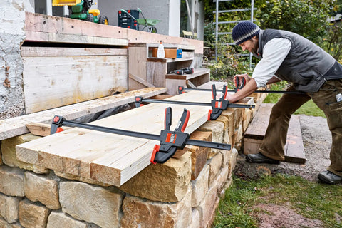 Person using Beefy 12 Inch Trigger Clamp Set With 600 Lb Clamping Force, Model EHKXL12, for woodworking outdoors.
