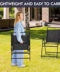 Woman carrying folded Outdoor Folding Patio Chairs Set Of 4 for the Backyard and Porch, lightweight and portable, black metal frames.