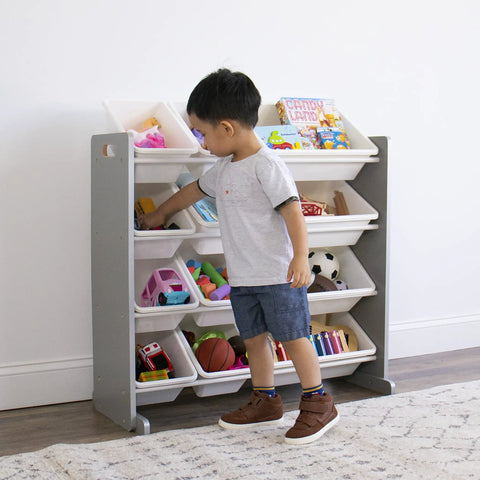 Child organizing toys in 12 bin toy storage organizer for kids playroom, 4-tier in grey and white with durable wood frame and steel dowels.