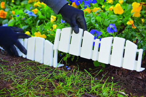 Hands installing No-Dig Landscape Edging Kit with anchoring spikes as 4.5 inch tall white wood-look garden border around flowers.