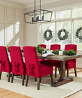 Dining room with red slipcovered chairs around wooden table, holiday wreaths on windows, and chandelier overhead.