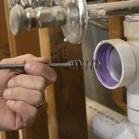 Person using Pro 50 Foot Heavy Duty Steel Drum Drain Auger Plumbing Snake for quick clog removal in visible pipe opening.