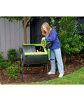 Person using 48 Gallon Geared Two Compartment Compost Tumbler for no hassle kitchen and yard waste turning, durable poly construction.