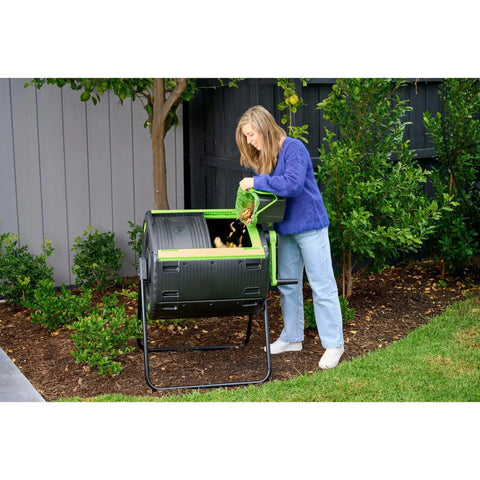 Person using 48 Gallon Geared Two Compartment Compost Tumbler for no hassle kitchen and yard waste turning, durable poly construction.