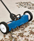 Rugged 18 Inch Magnetic Floor Sweeper With Big Wheels Rolling Smooth On Asphalt Concrete Grass And Gravel Fast Dump Lever and Removable Handle collecting metal scraps on a garage floor.