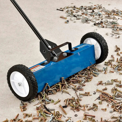 Rugged 18 Inch Magnetic Floor Sweeper With Big Wheels Rolling Smooth On Asphalt Concrete Grass And Gravel Fast Dump Lever and Removable Handle collecting metal scraps on a garage floor.