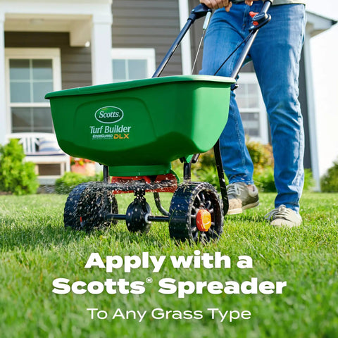 Person using a green Scotts Turf Builder spreader on a lawn