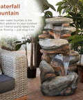 40-Inch Four Tier Rock Floor Fountain With Cascading Water And White LED Lights in a natural garden setting.