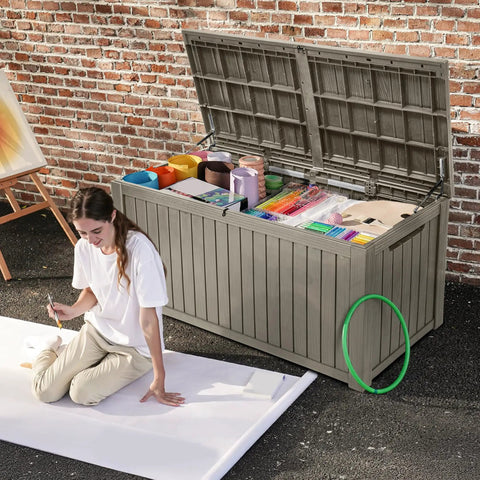 Beefy 220 Gallon Outdoor Deck Storage Box with Removable Divider, light brown, open with art supplies visible, woman sitting nearby