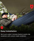 Man relaxing in a hammock under 12x10 Rain Fly Tarp For Survival Camping, Ultra Lightweight Waterproof Shelter with durable 210T polyester.