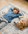 Child and dog lying on a decorative rug on a hardwood floor.