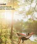 Person relaxing in a hammock by a lake with sunlight filtering through trees, enjoying nature.