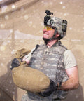 Person in military uniform with sandbag in dusty outdoor setting