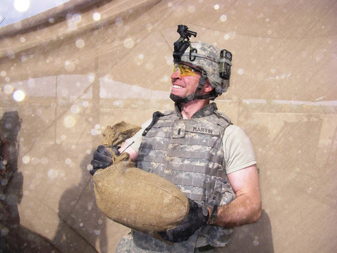 Person in military uniform with sandbag in dusty outdoor setting