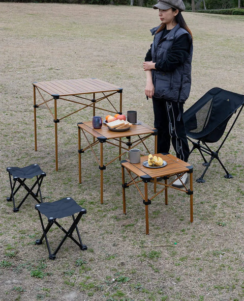 Ultra Lightweight Stable Folding Aluminum Table With Roll Up Top And Carry Bag For Camping Picnics Beach Chill Backyard Barbecues Tailgating And RV Trips Anywhere shown setup outdoors with chairs and food items.