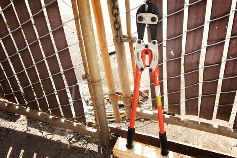 24 Inch PowerPivot Center Cut Double Compound Action Bolt Cutter with induction hardened blades against a metal fence.