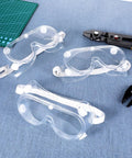 Three clear Ten Pack Anti Fog Lab Goggles Over Glasses Safety Eyewear with Soft Silicone Lenses on blue surface with tools.