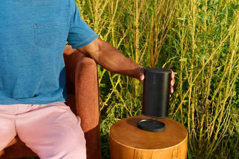 Person placing Take Anywhere Portable Bluetooth Speaker With WiFi Alexa Built In 24 Hour Battery Life on a wooden table outdoors