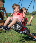 Children playing on web swing of Cedar Cove Wooden Swing Set With Spiral Tube Slide And Wave Slide for backyard playtime