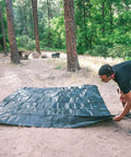Two people setting up Medium Duty Ripstop Camping Tarp 6 By 8 Feet Waterproof Cover Dark Green 5 Mil Thick With Reinforced Grommets