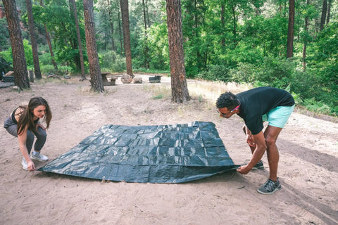 Two people setting up Medium Duty Ripstop Camping Tarp 6 By 8 Feet Waterproof Cover Dark Green 5 Mil Thick With Reinforced Grommets