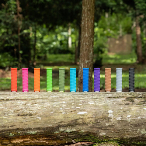 Colorful mountain bike grips on a log in forest, showcasing Holeshot Lock On Mountain Bike Grips With 22mm Inner Diameter.