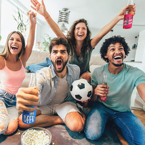 Four friends cheering on a couch with Neoprene can coolers in a living room, Snag This Awesome Bulk Set Of Eight Different Funny Quote Insulated Neoprene Can Coolers That Collapse For Easy Storage Great For Keeping Your Soda And Beer Cans Cold At BBQs Parties And More visible.