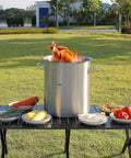 Outdoor scene of 42 Quart Stainless Steel Stock Pot With Strainer, Lid And Handles, Heavy Duty Commercial Grade with turkey on table.