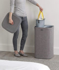 Person removing wash bag from Tota Laundry Hamper With Dual Compartments And Lid, 60 Liter Separation Basket in gray by a bed.