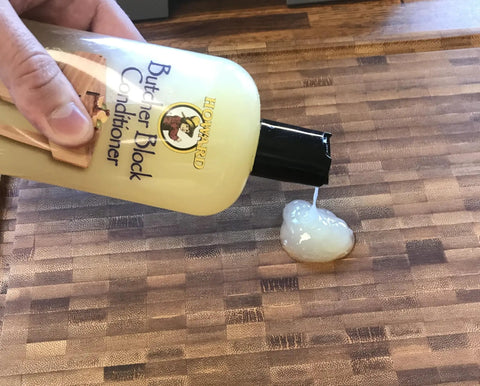 Deep Penetrating Food Grade Butcher Block Conditioner poured on wooden surface with hand holding bottle