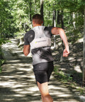 Back view of a man running with ultralight running hydration vest with two 500ml TPU soft flasks on forest trail.